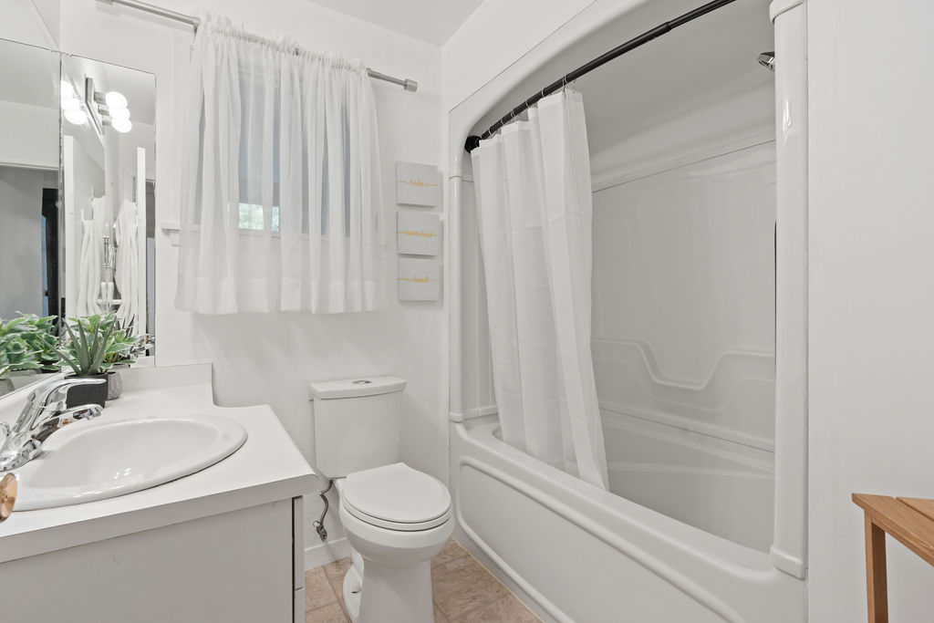 A white bathroom with a small window above the toilet with an airy curtain