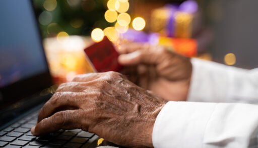 a photo of a person's hands typing on a computer while holding a credit card with holiday lights in the background