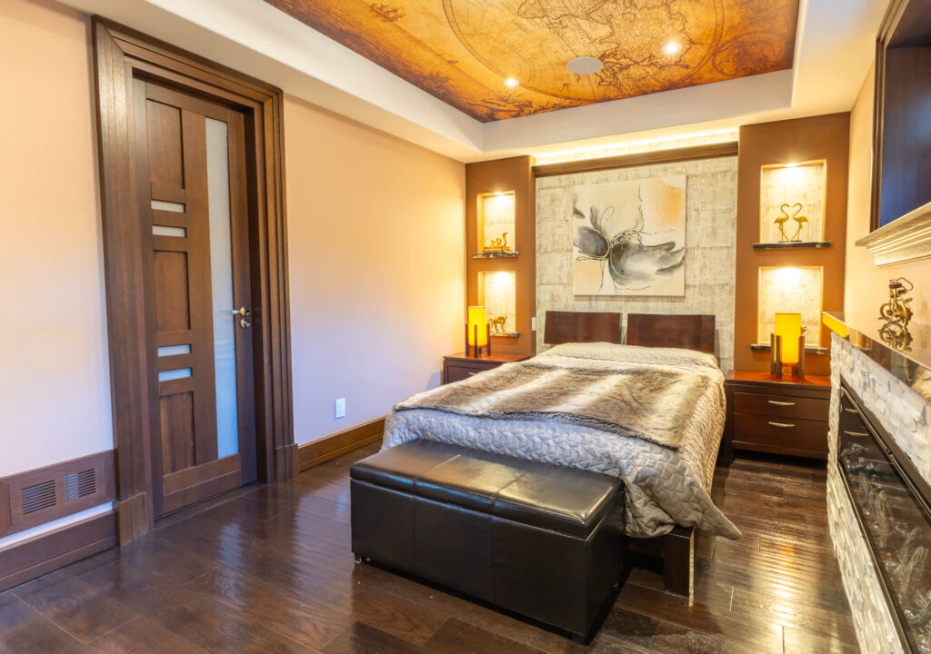 A white bed with a furry blanket. At the end of the bed, a black stool