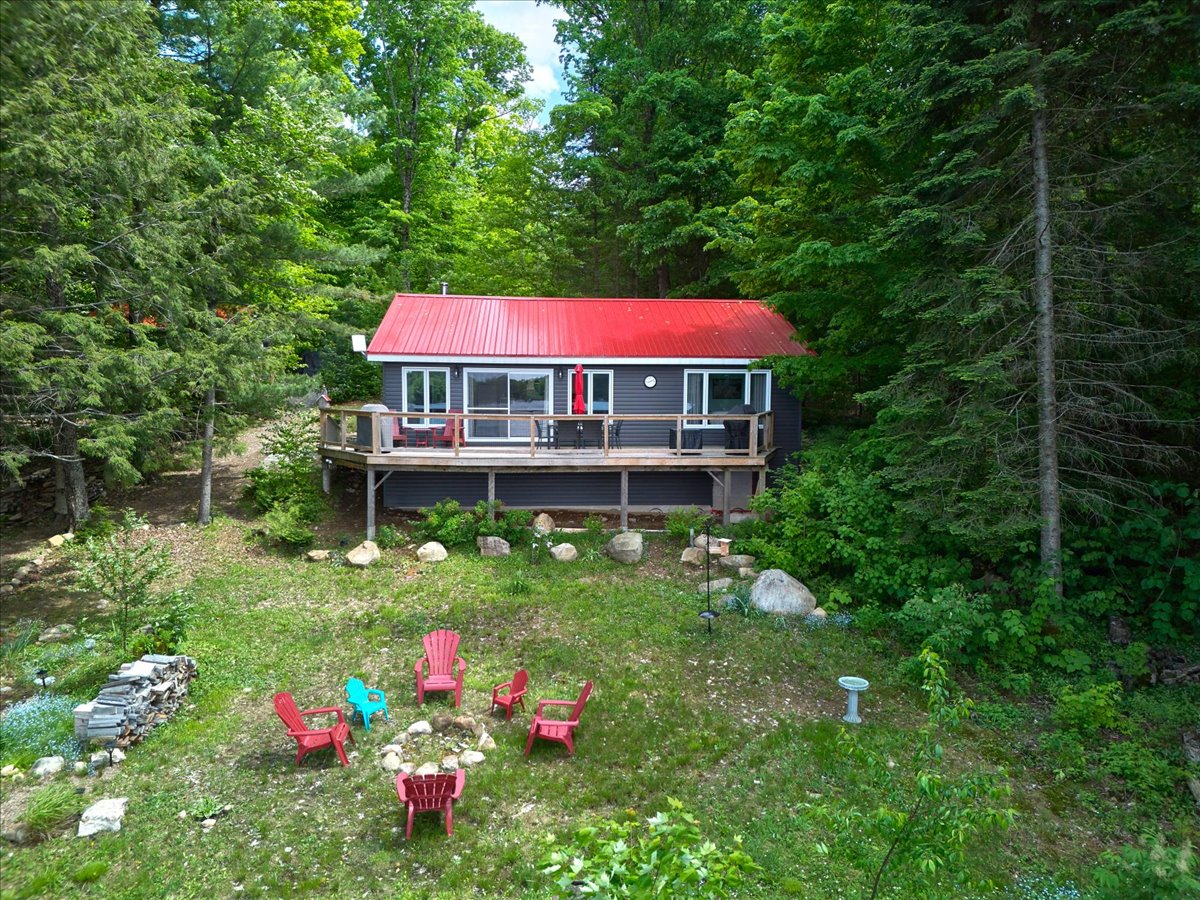 A grey paneled cottage with a red roof next a spacious green lawn with a fire pit
