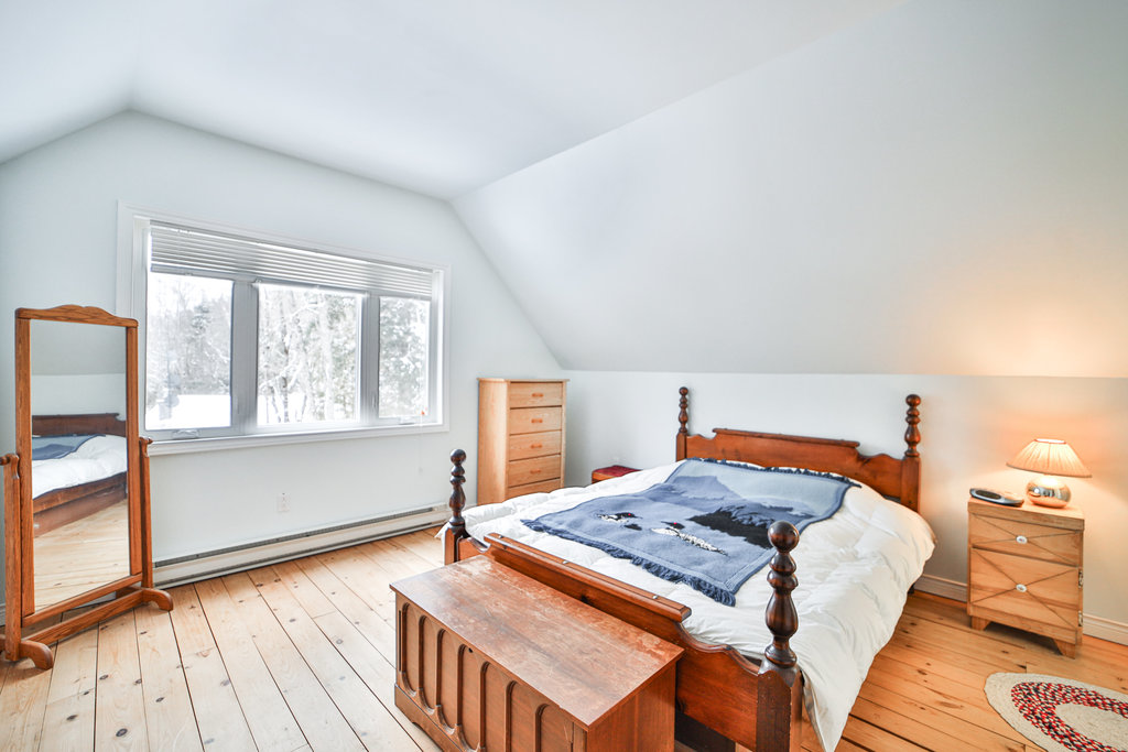 A white bed on a wood bedframe with a blue blanket in a white room
