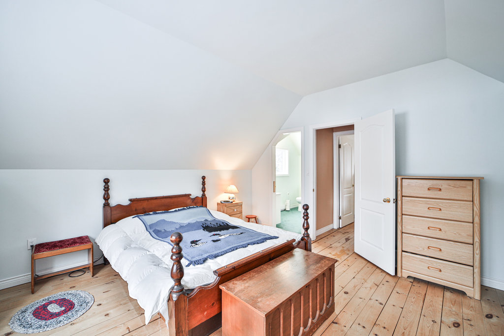 A white bed on a wood bedframe with a blue blanket in a white room
