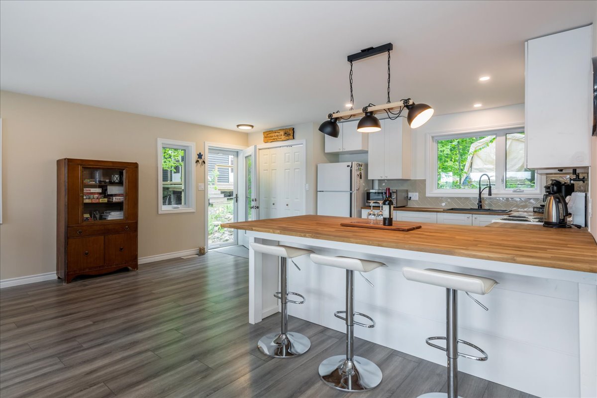 A spacious kitchen with grey hardwood floors. A white kitchen island with three barstools