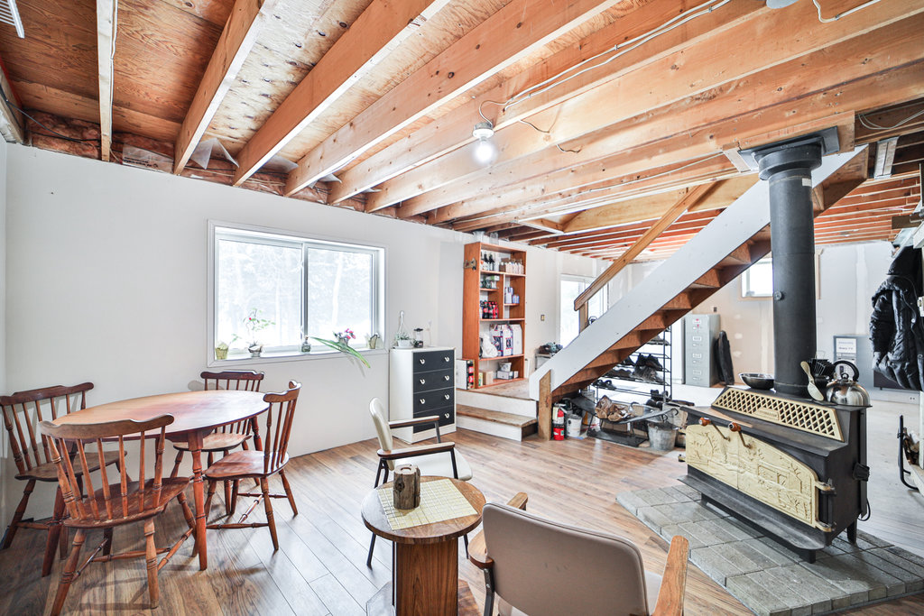 A small round dining area next to a small chair facing a wood stove in an unfinished basement