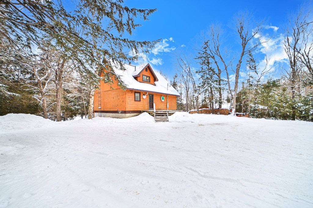 A red-brown wood cabin sits on a snowy property