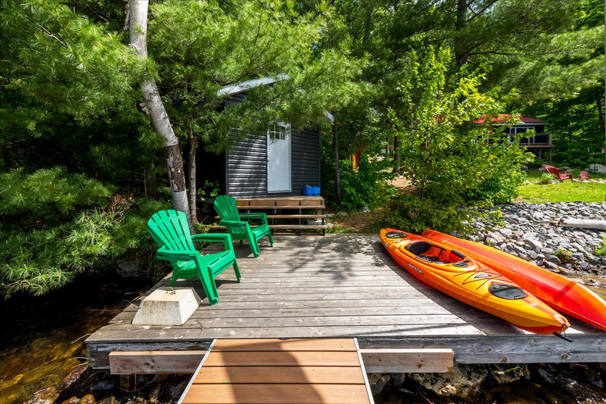 A deck with two green Muskoka chairs and an orange kayak