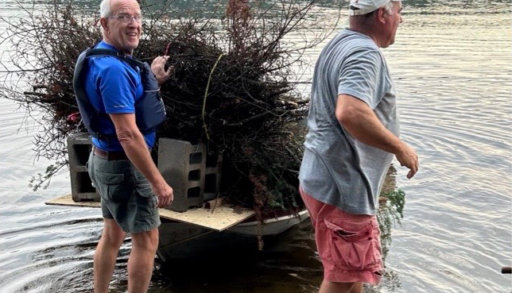 Two men in the lake with a boat full of sticks