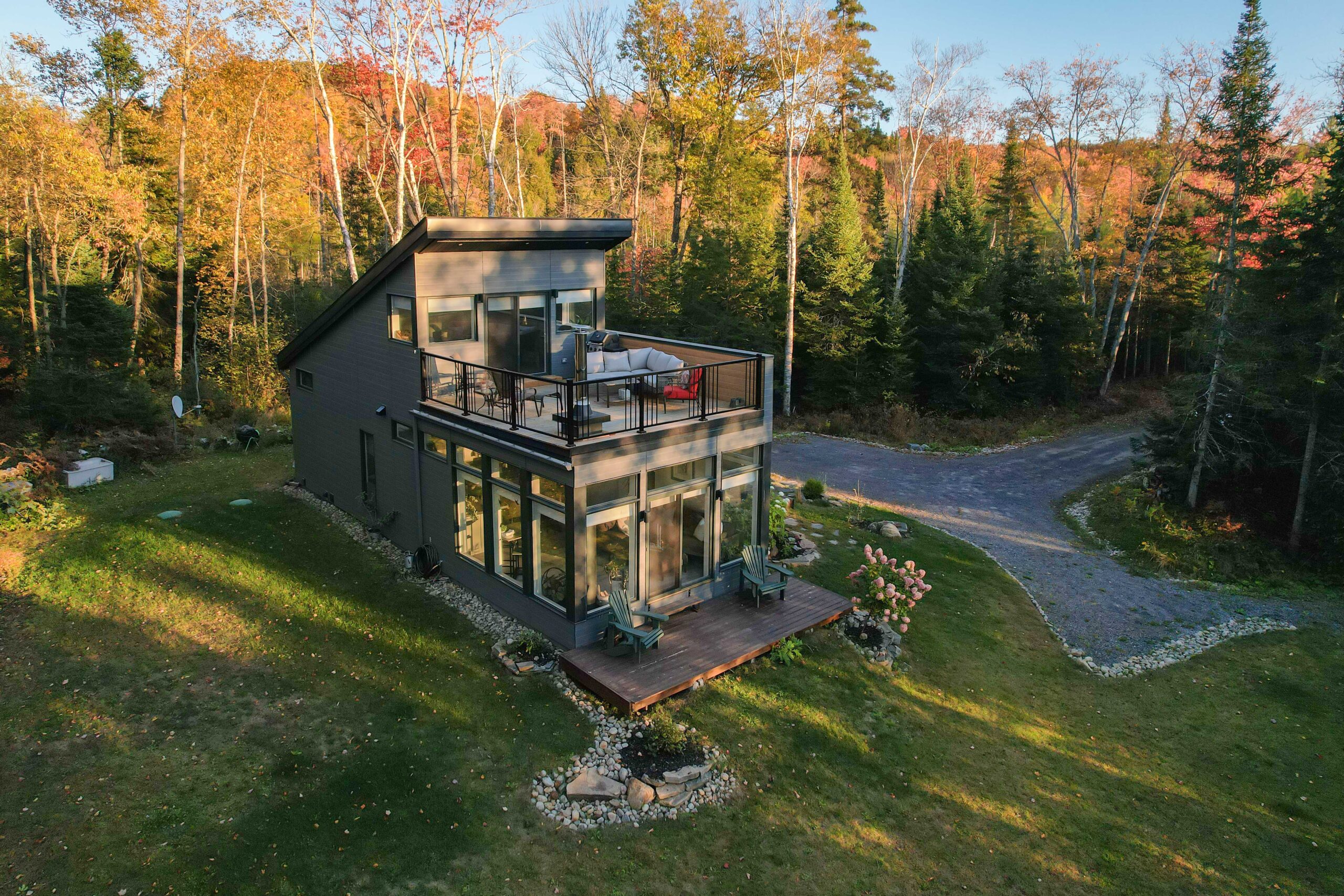A dark grey cottage with a second-story deck on a large grassy property