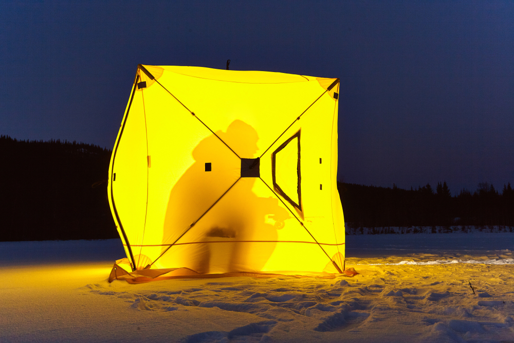 A yellow ice fishing hut with a person inside, in darkness