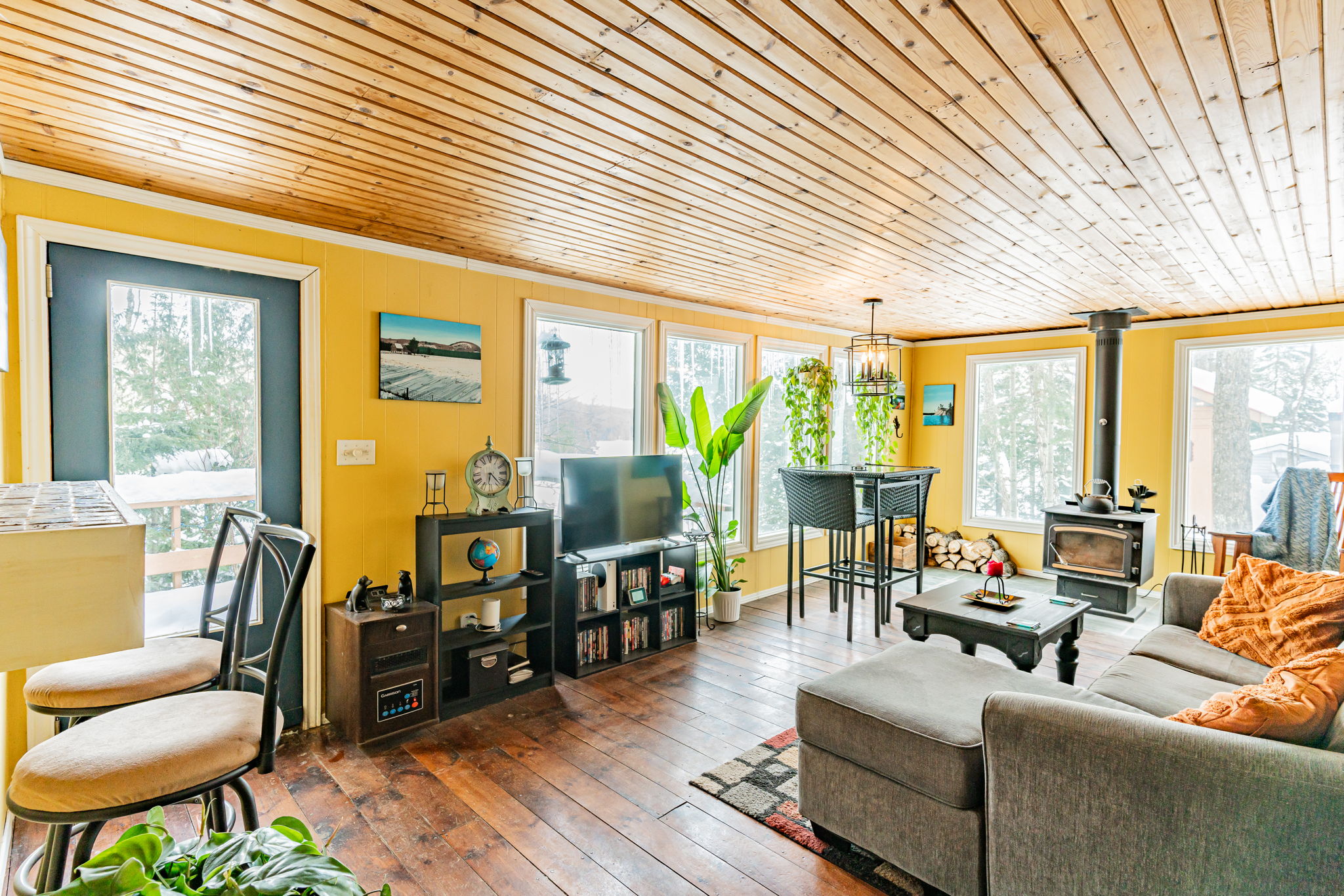 A spacious yellow living space with a grey couch and high-top dining set