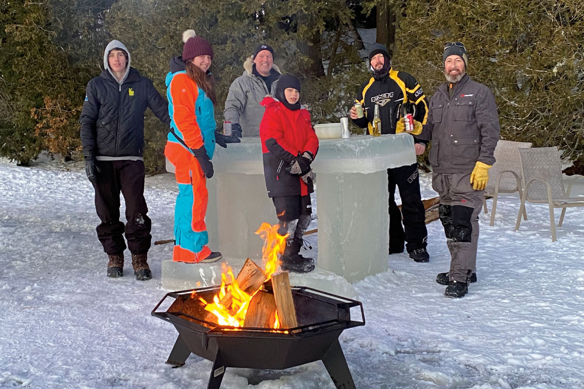 a group of people in snowsuits tand around a bar made of ice