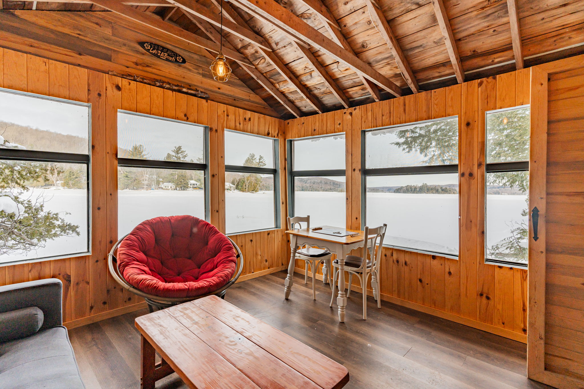 A red papasan next to a two-person dining set in a wood room with huge windows