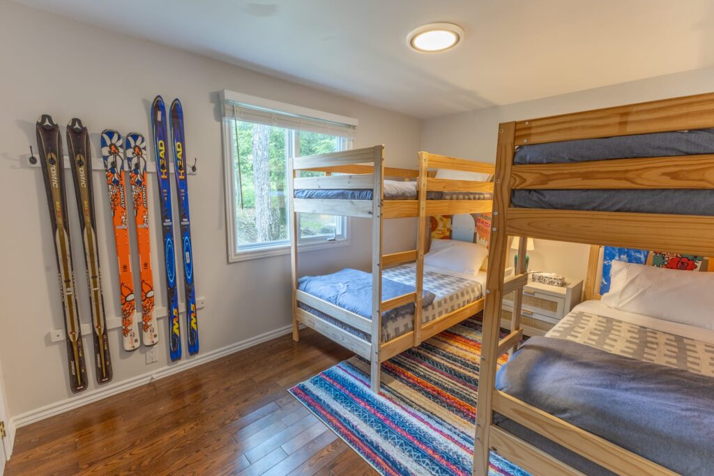 Two bunk beds with patterns bedspreads on a striped carpet. Decorative skis hang on the walls