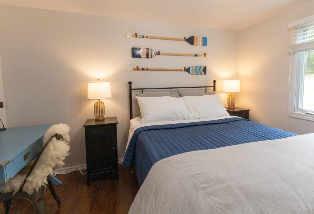 A bed with blue covers. On the wall behind, decorative canoe paddles hang