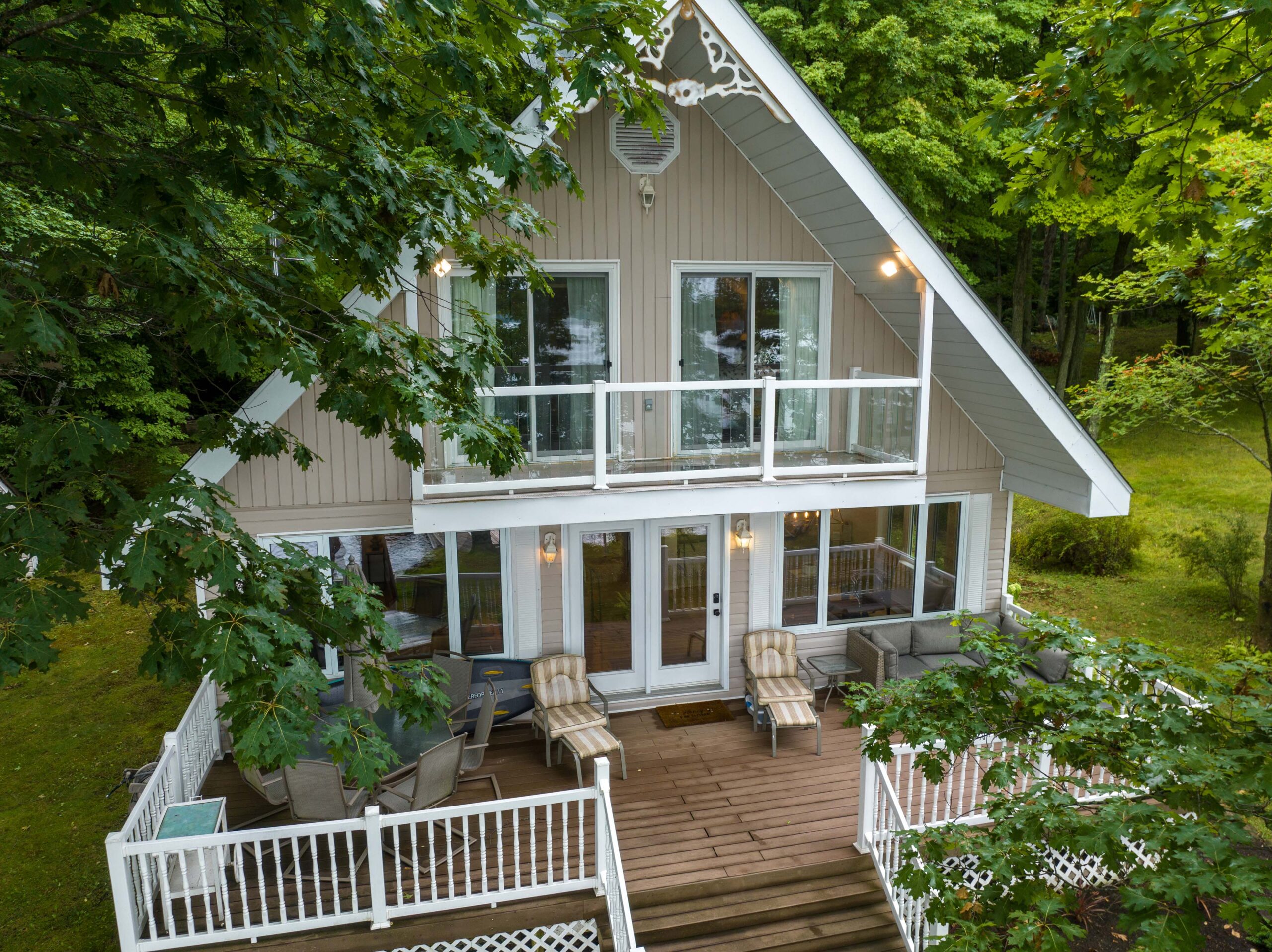 A beige cottage with white trim. On the lower level deck, two brown lounge chairs.