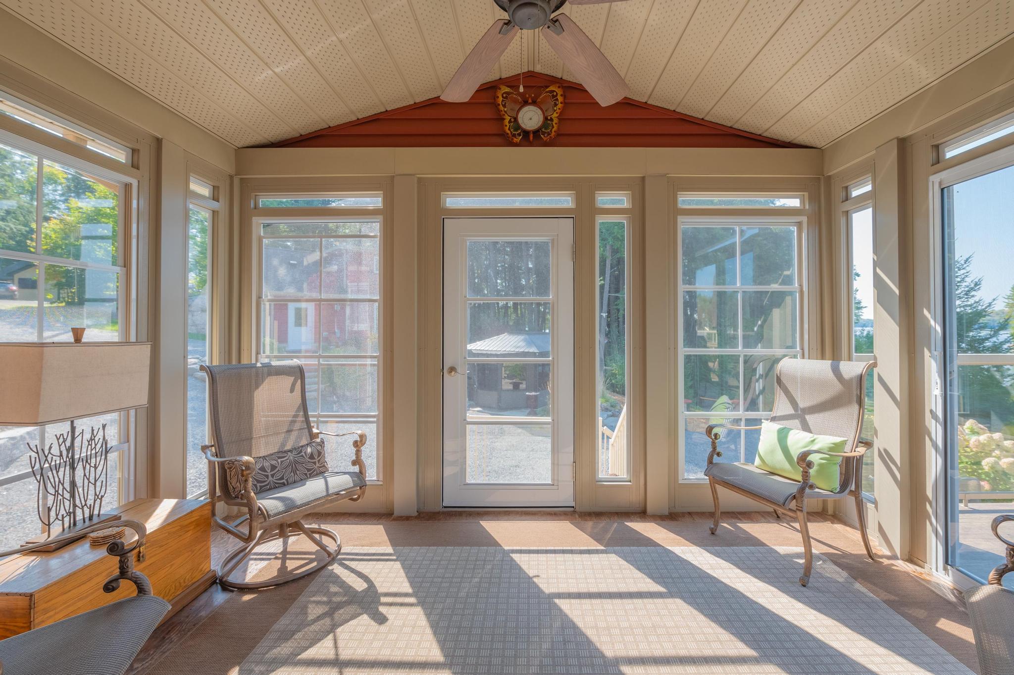 A bright sunroom with floor-to-ceiling windows, offering panoramic views of the lake and surrounding trees.