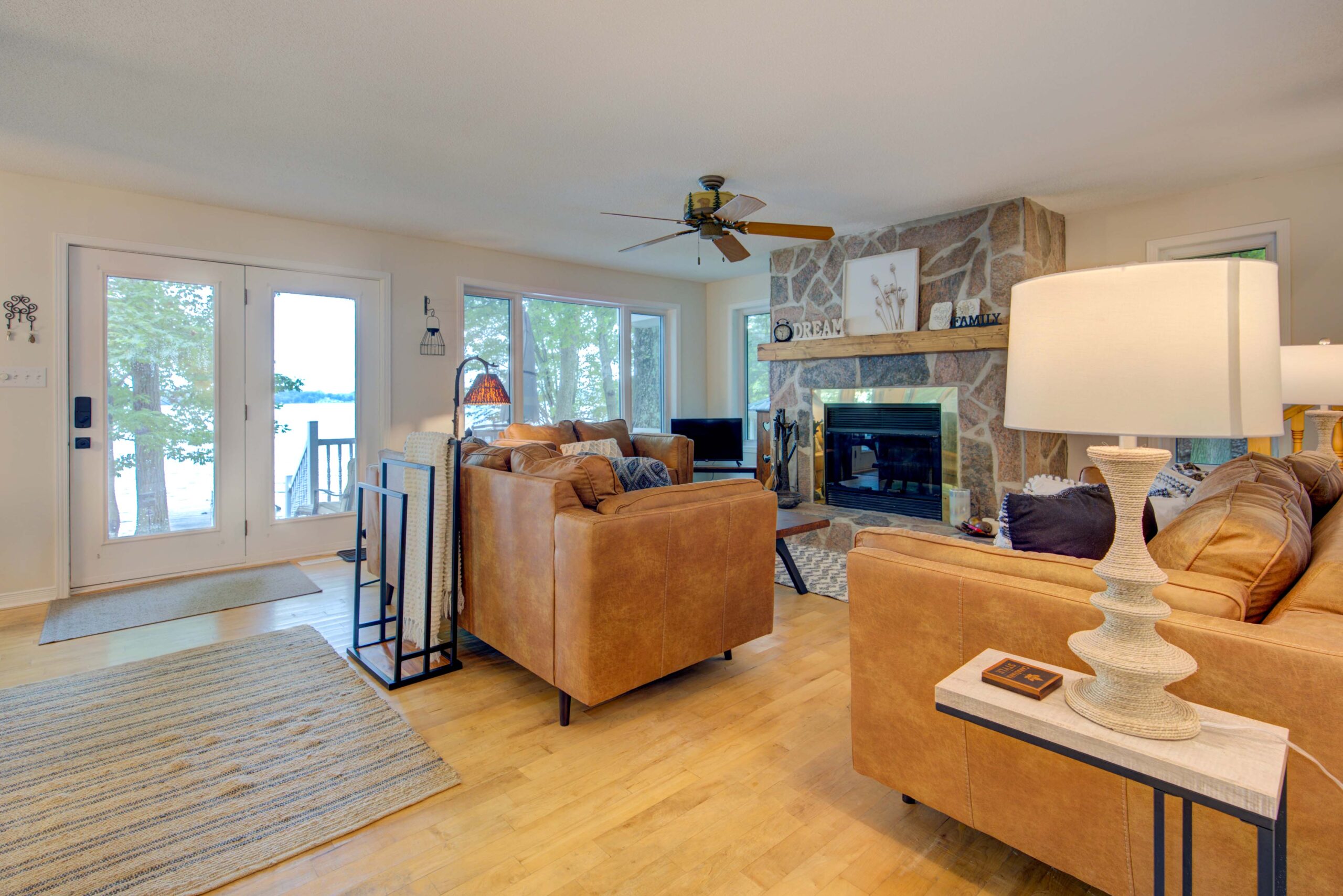 Brown suede couches in an open-concept living room. One the far wall, bright windows with viewsof the lake.