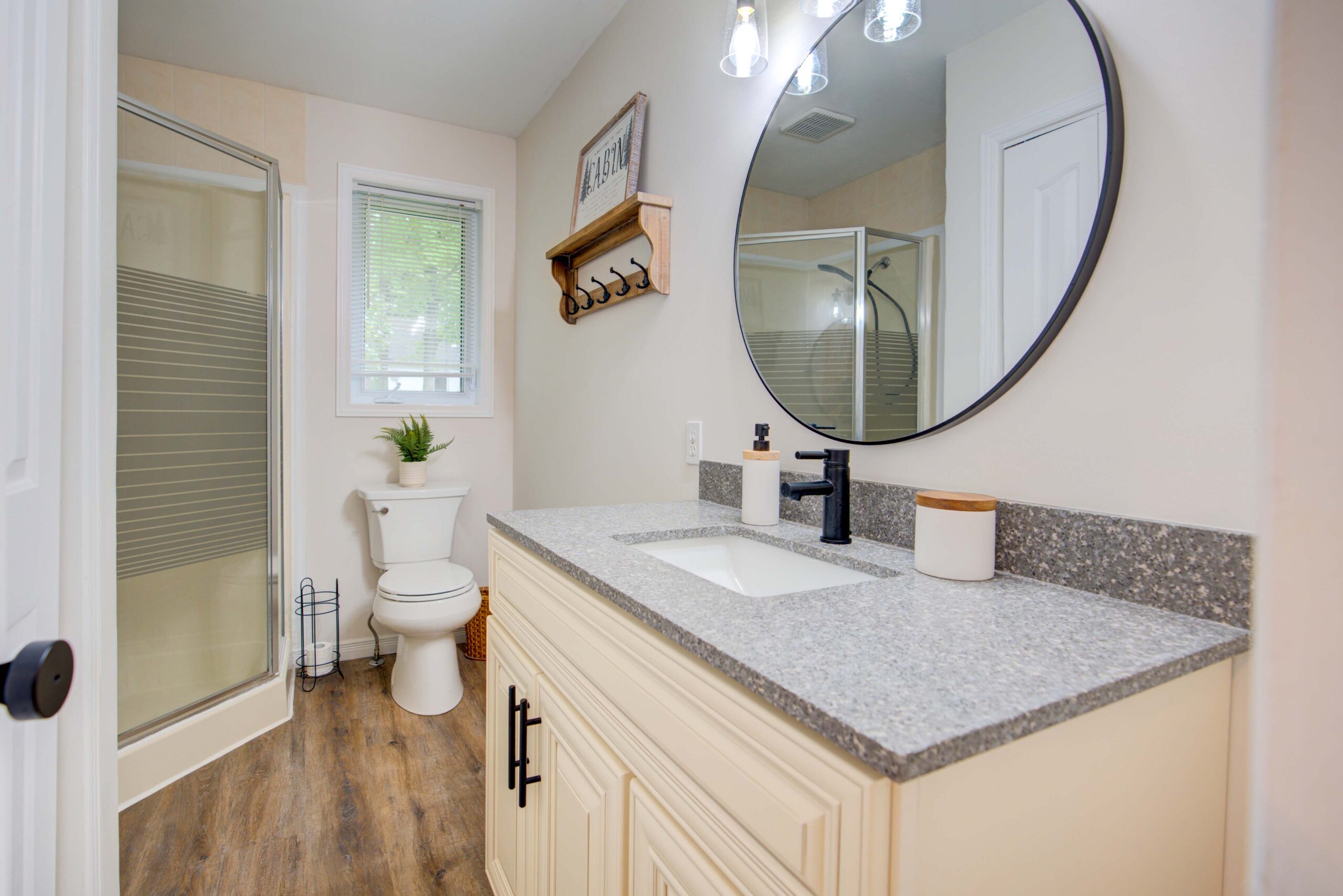 A white bathroom with white cabinets and a round mirror