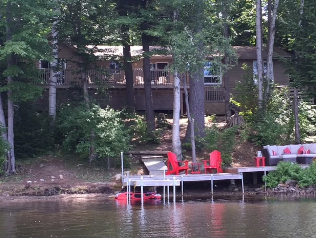 Stone steps in a forest lead down to a dock with red Muskoka chairs