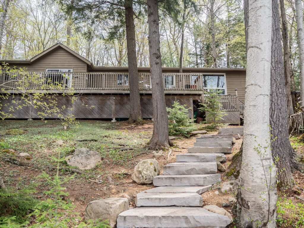 Stone steps lead up to a grey paneled cottage