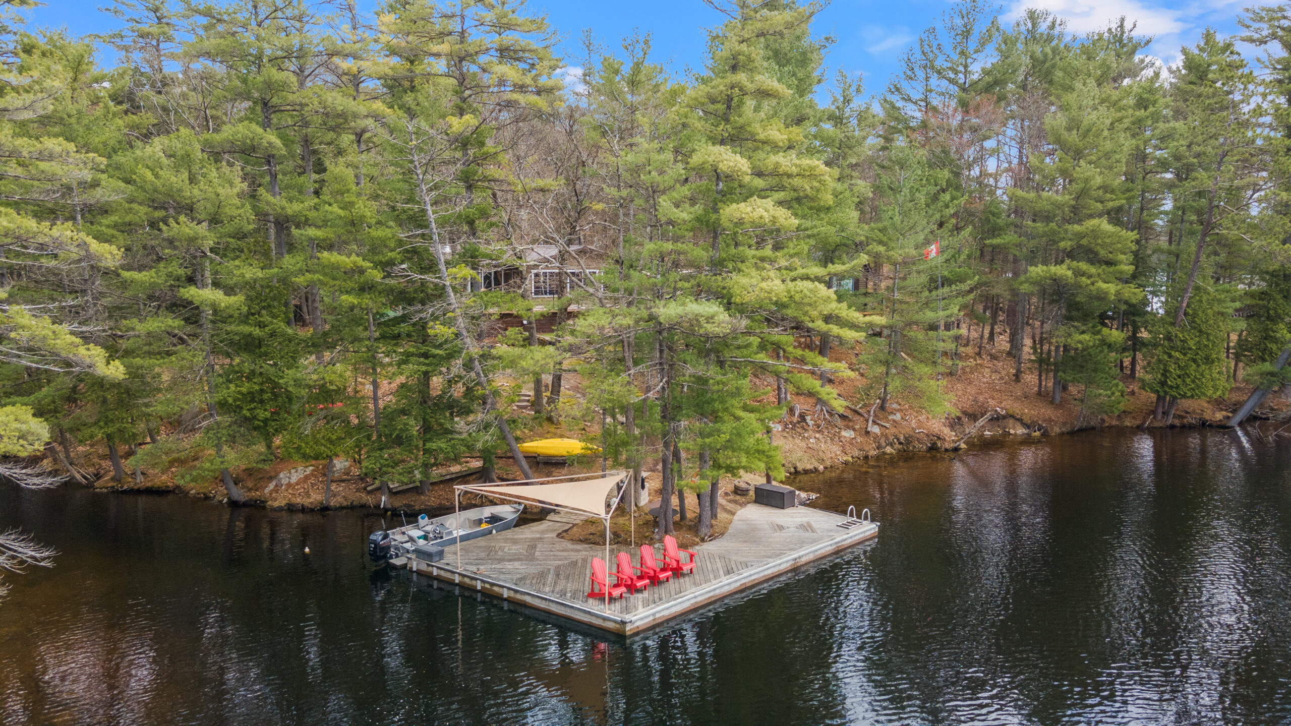 A square-shaped dock with red muskoka chairs in a forest