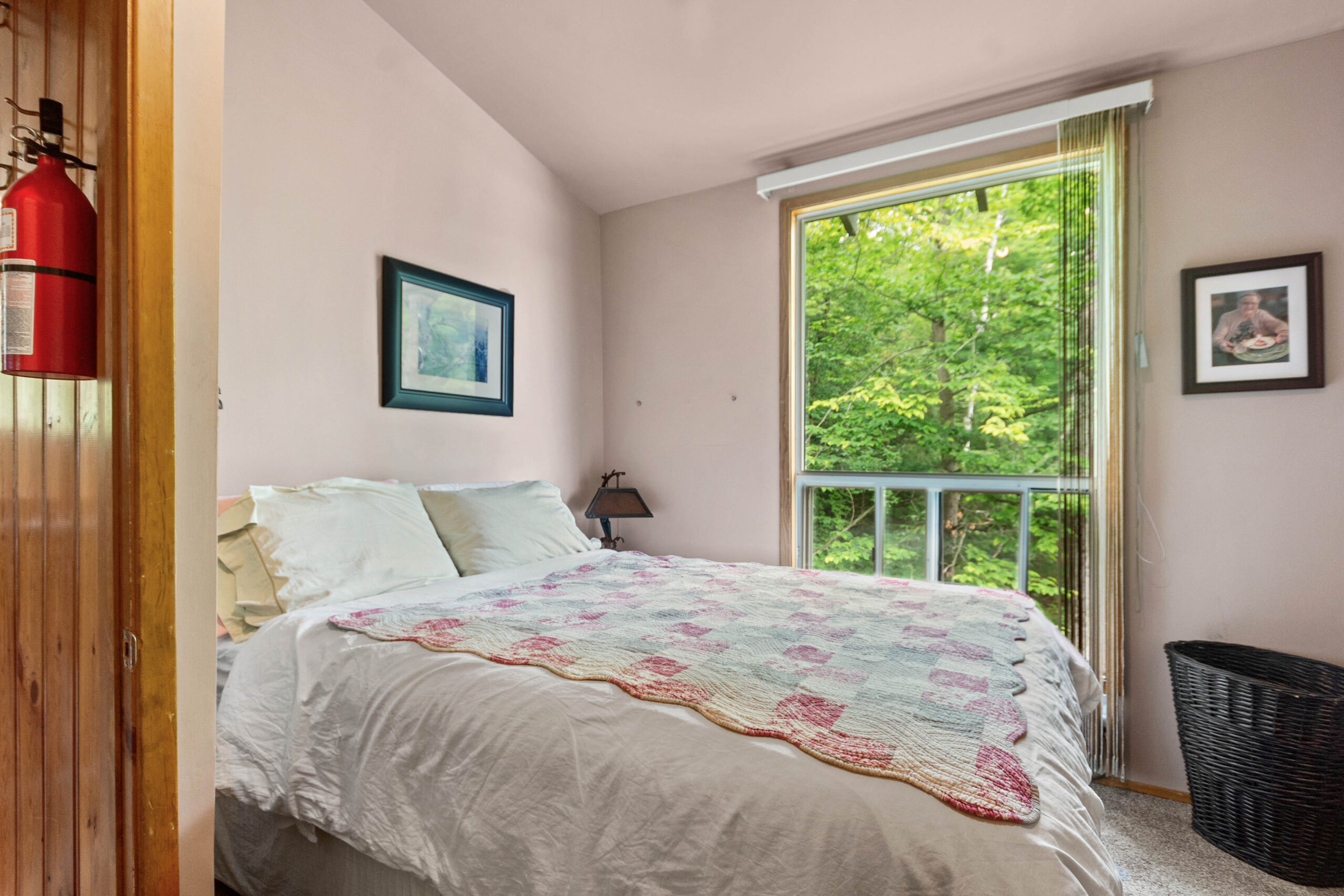 A white and pink bed in a white room with a large window