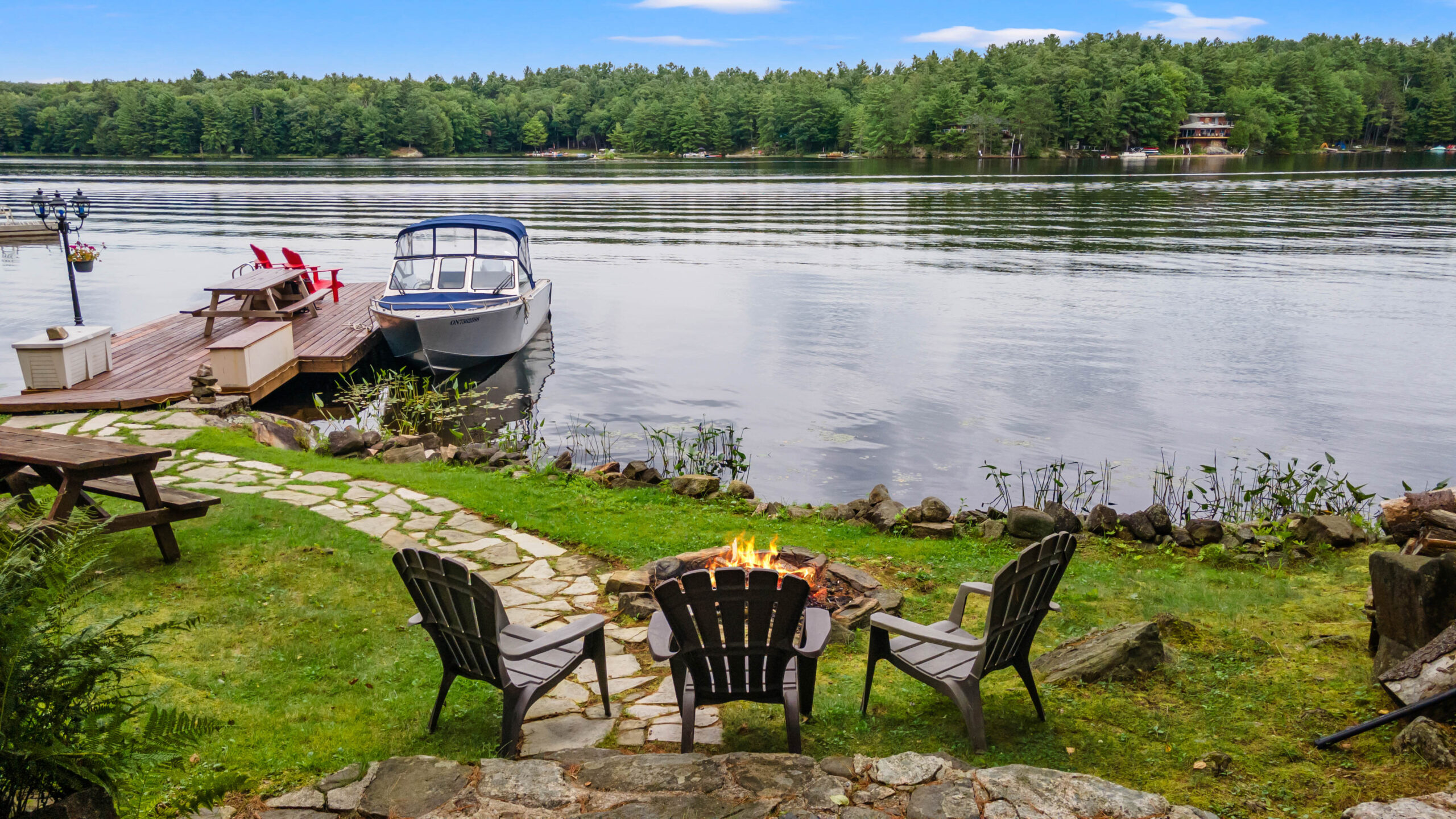Three Muskoka chairs face a fire pit in front of the lake
