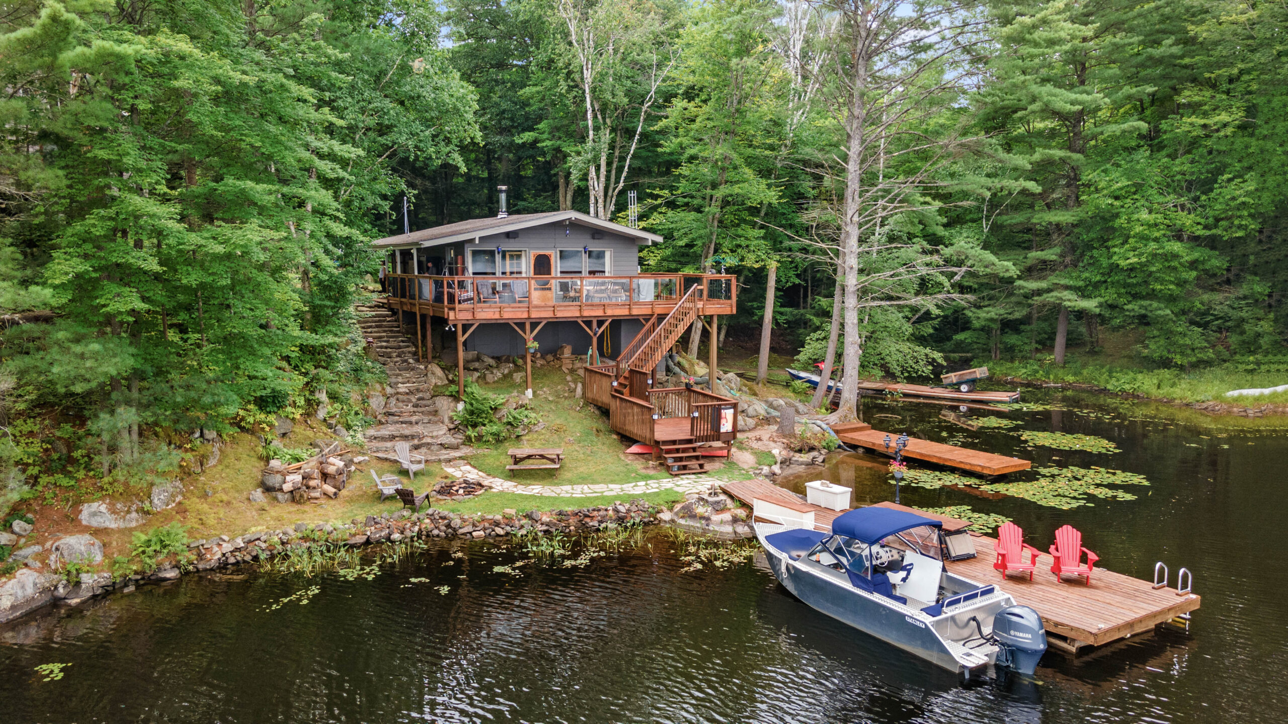 A grey cottage on stilts set back from a lake