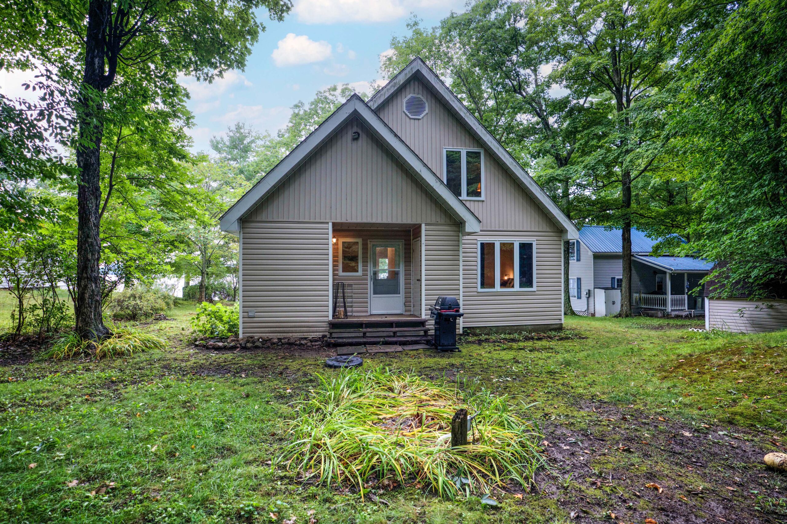 The outside entryway to a beige paneled cottage in the forest.