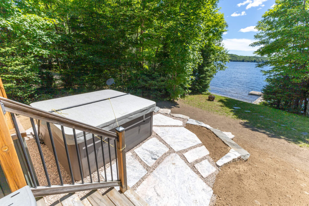 A closed hot tub on a stone patio faces the lake