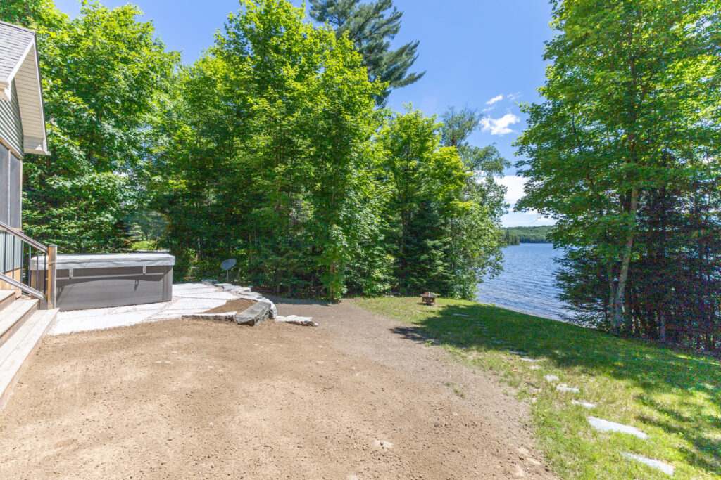 A closed hot tub on a stone patio on a dirt yard faces the lake