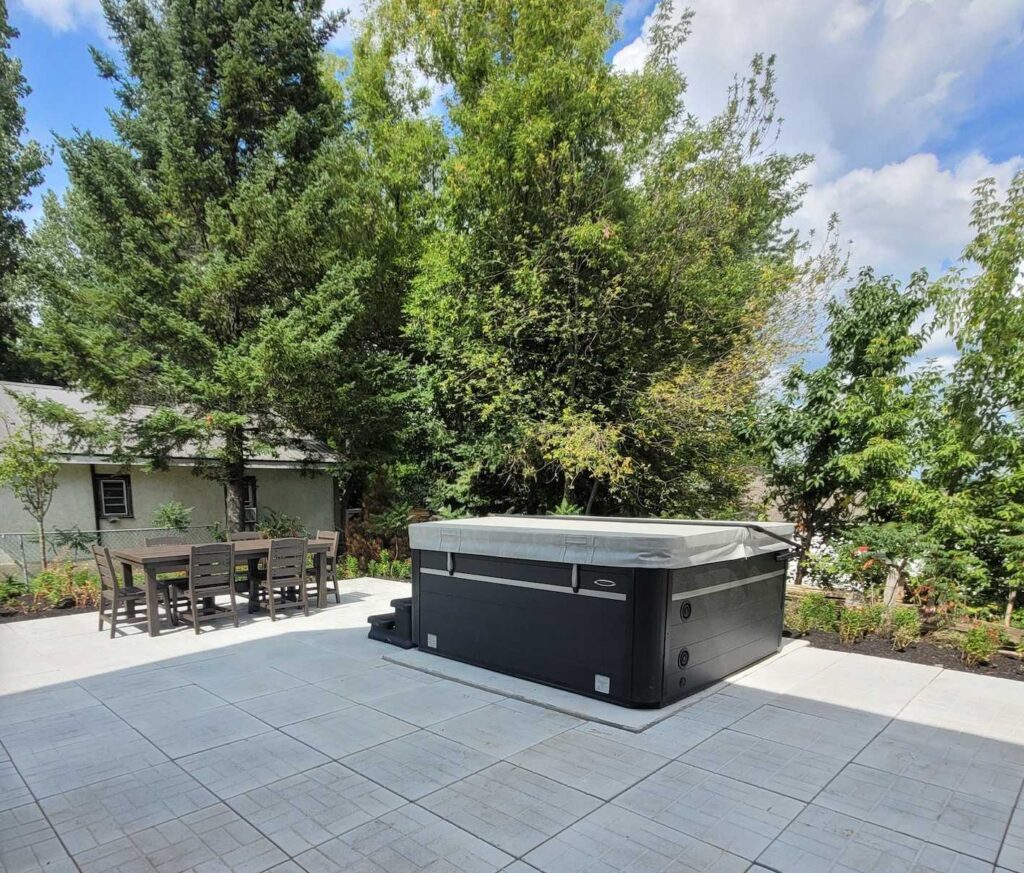 A closed hot tub on a stone patio with trees behind