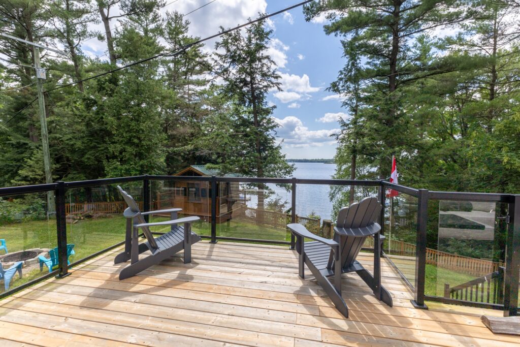 Two black Muskoka chairs face out towards the lake on a deck