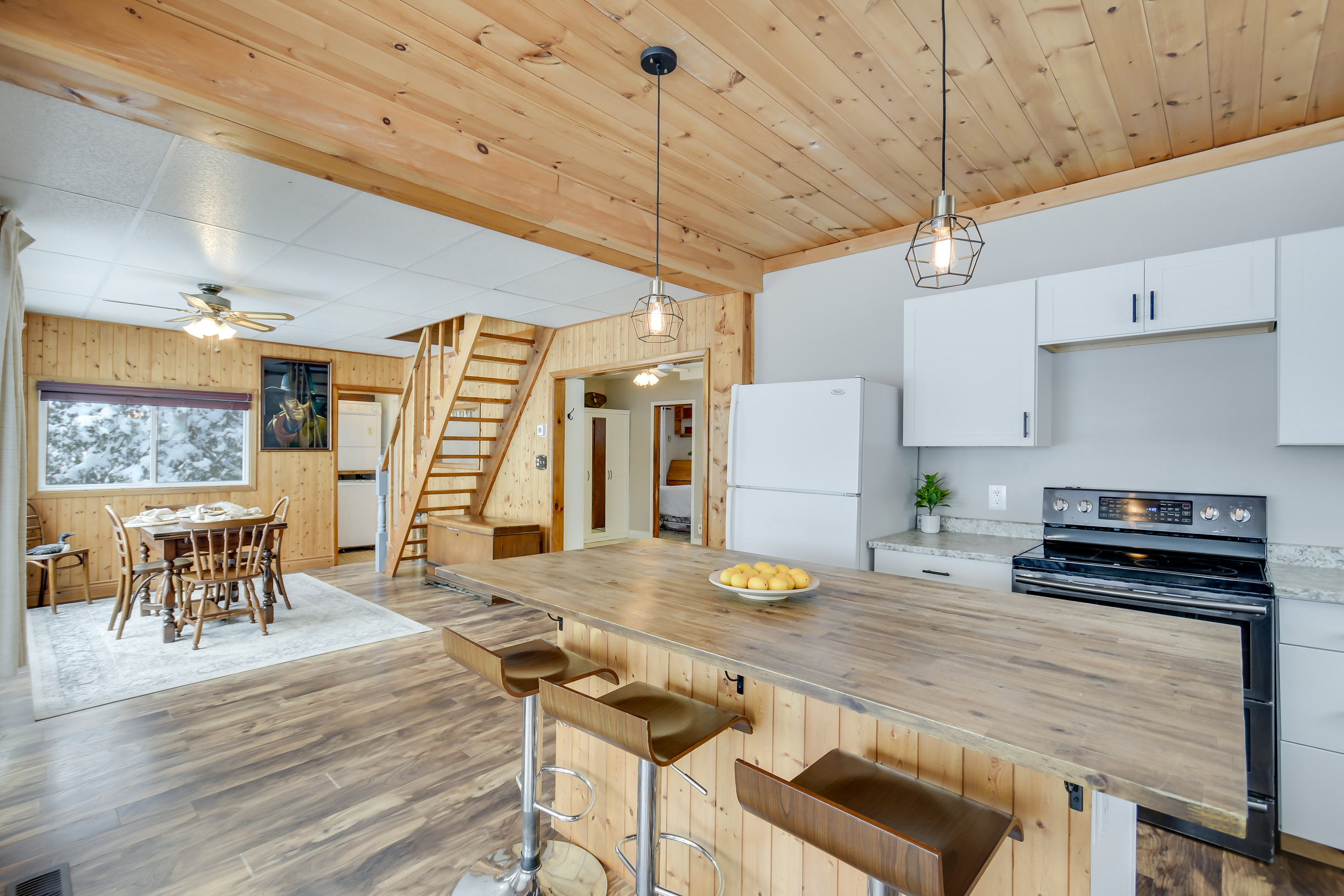 A beautifully updated open-concept kitchen with wood-paneled ceilings, modern white cabinetry, pendant lighting, and a large island with bar seating.