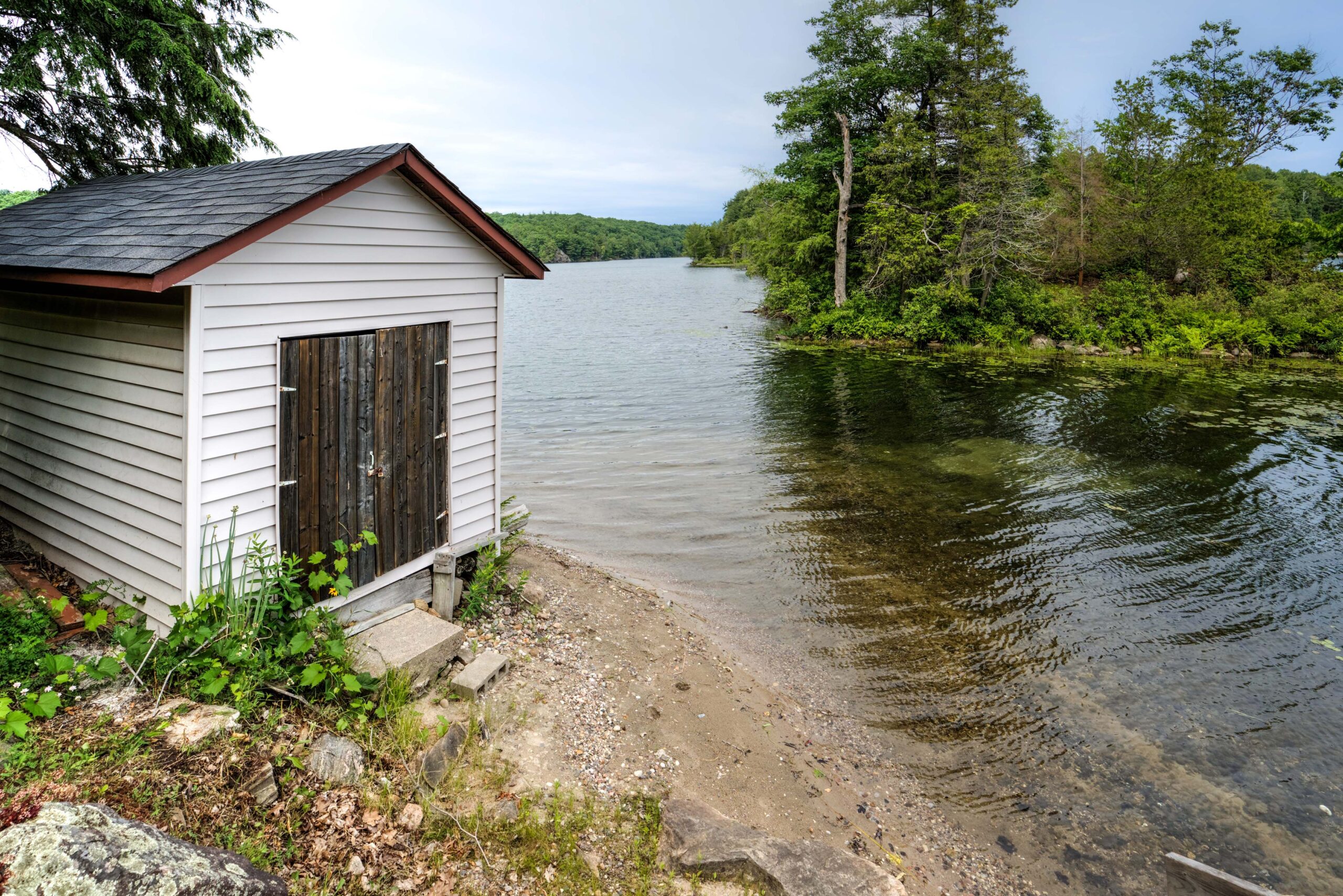 A white wood-paneled shed with a brown door by the sandy beach