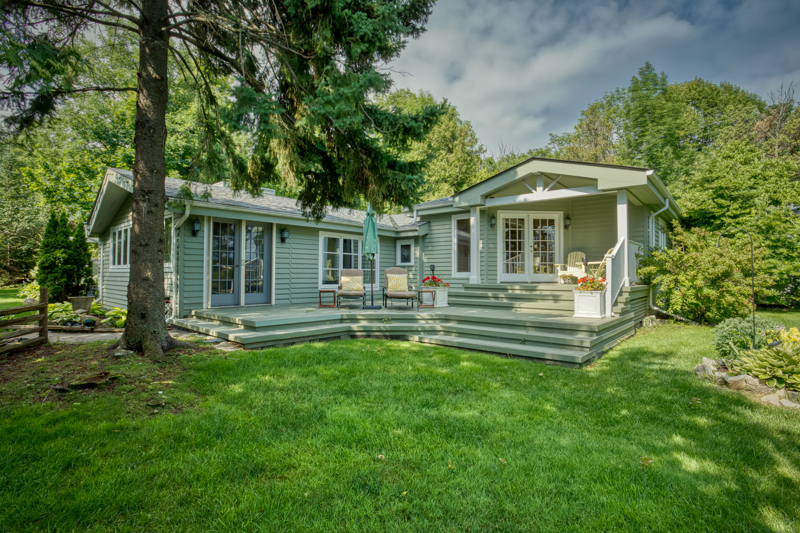 A green-paneled cottage with white trim and steps to a grassy lawn