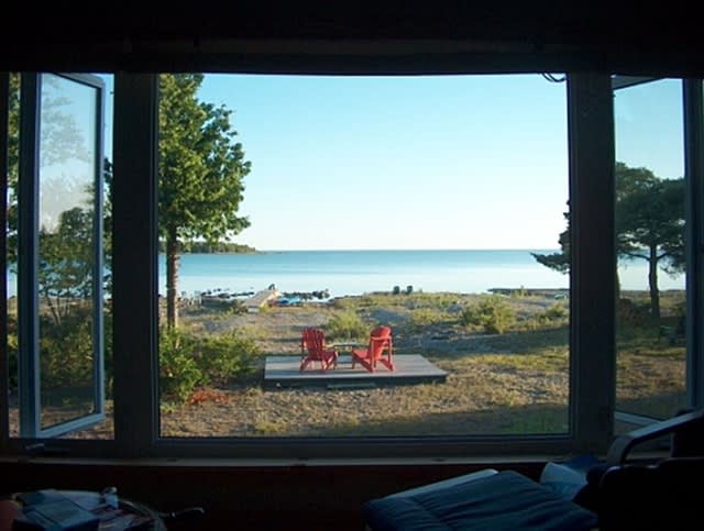 A bright window looks out at two red Muskoka chairs facing the lake