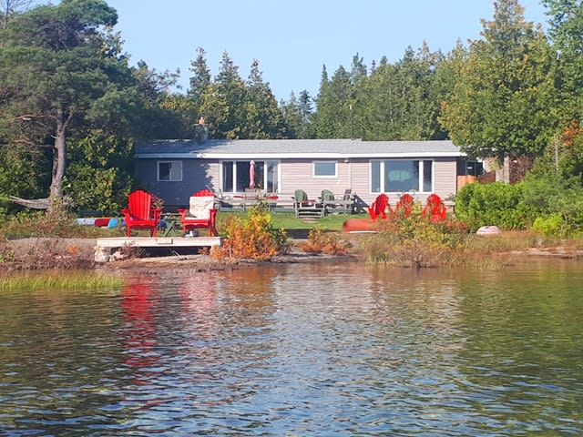 A light grey cottage with red Muskoka chairs in front