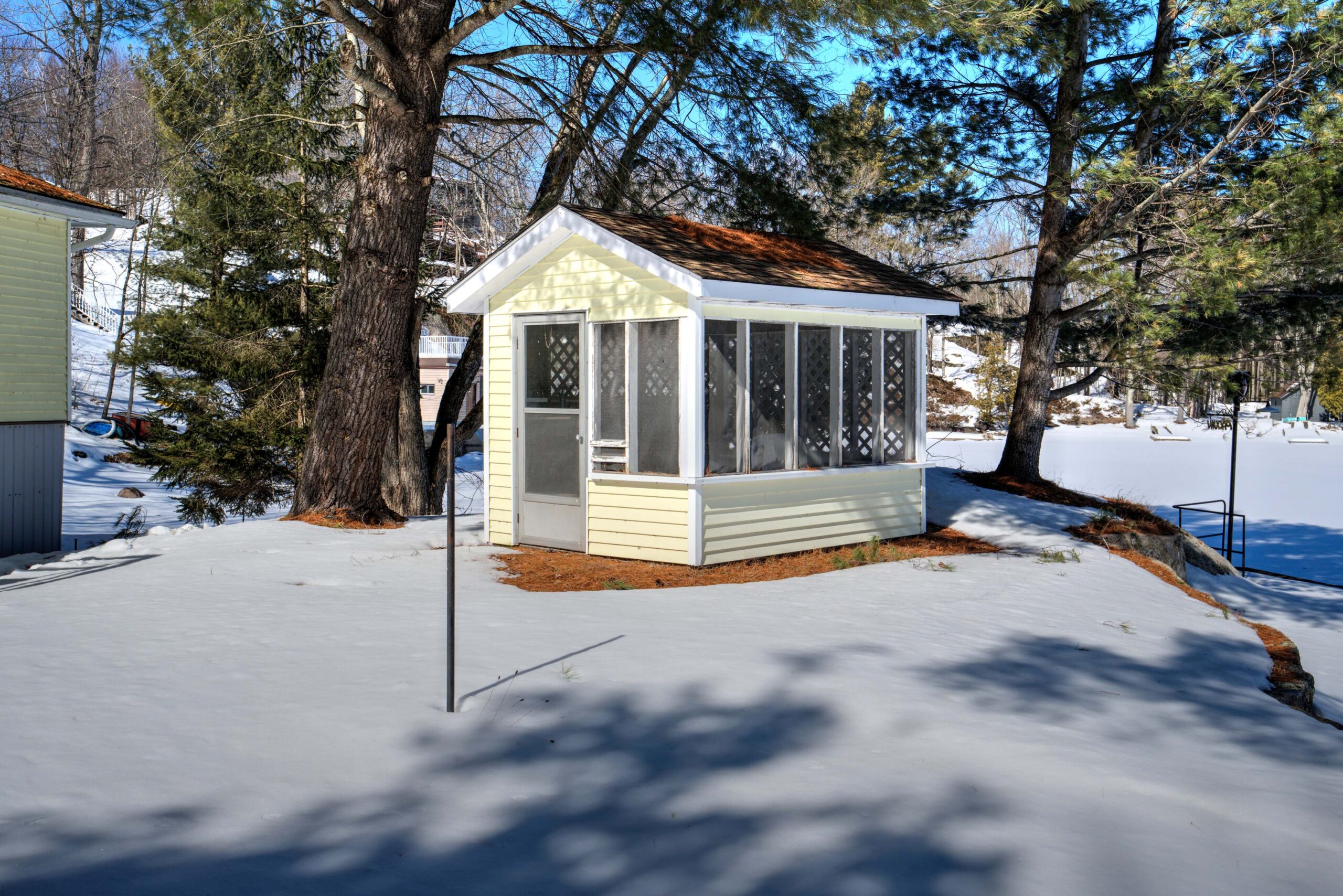 A small yellow-paneled gazebo on a snowy lawn
