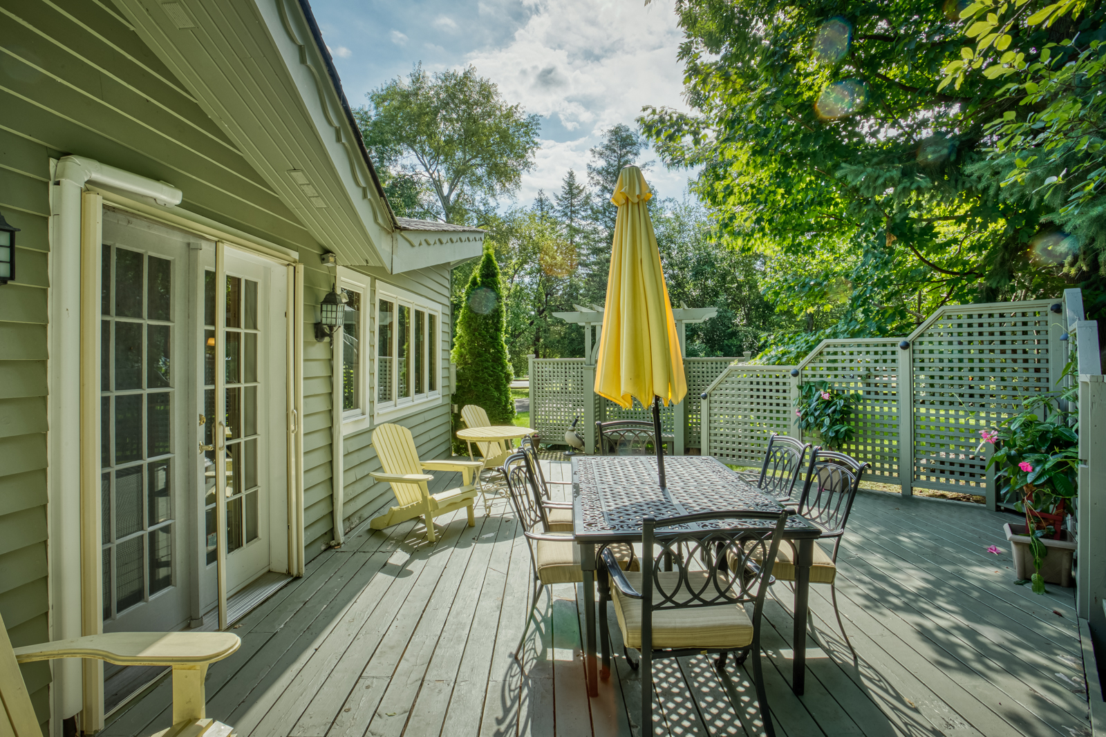 A green-paneled deck with a glass dining table. On the table, a closed yellow umbrella