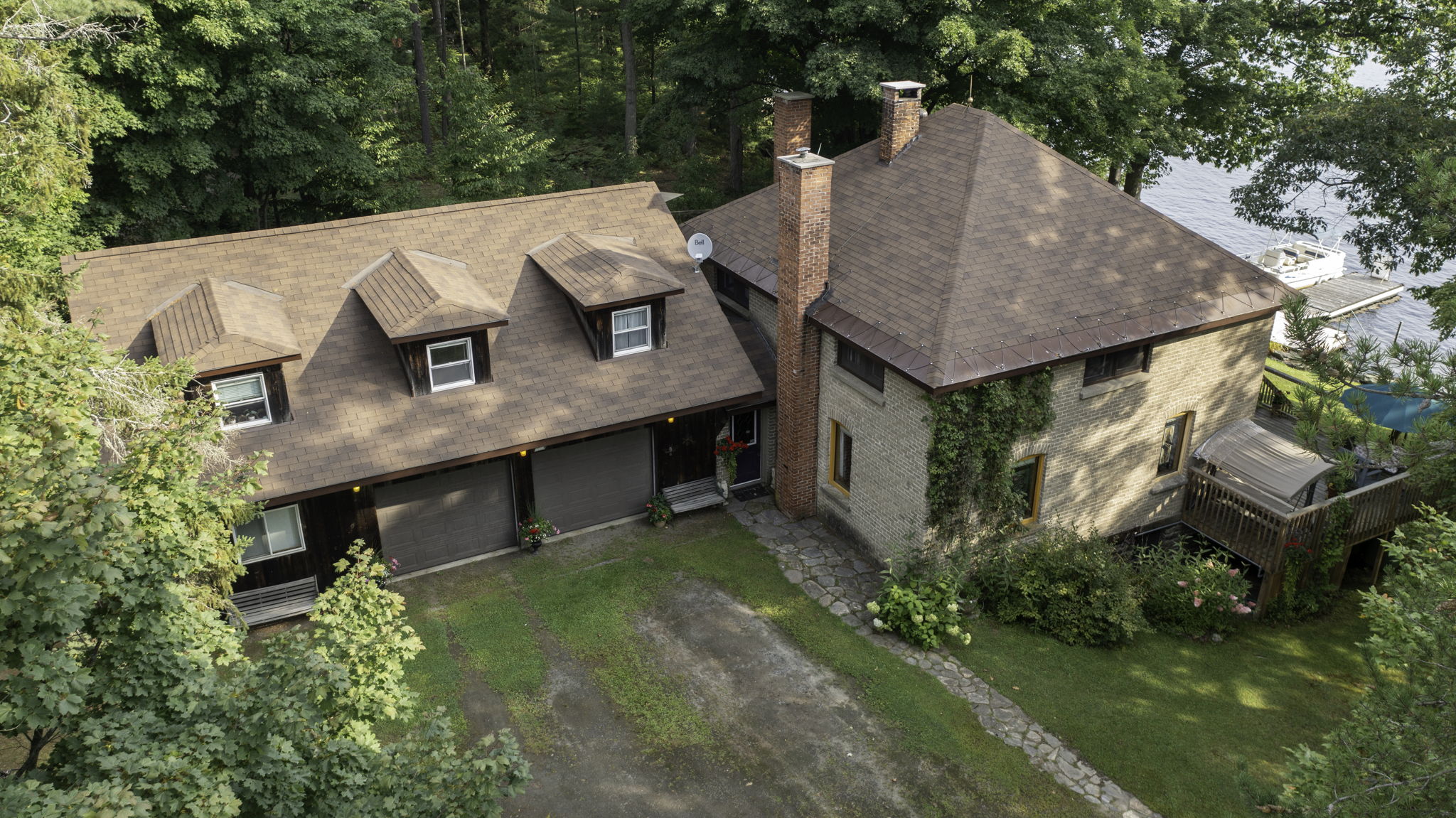 Overhead view of farmhouse, decks, and wooded lot leading to waterfront