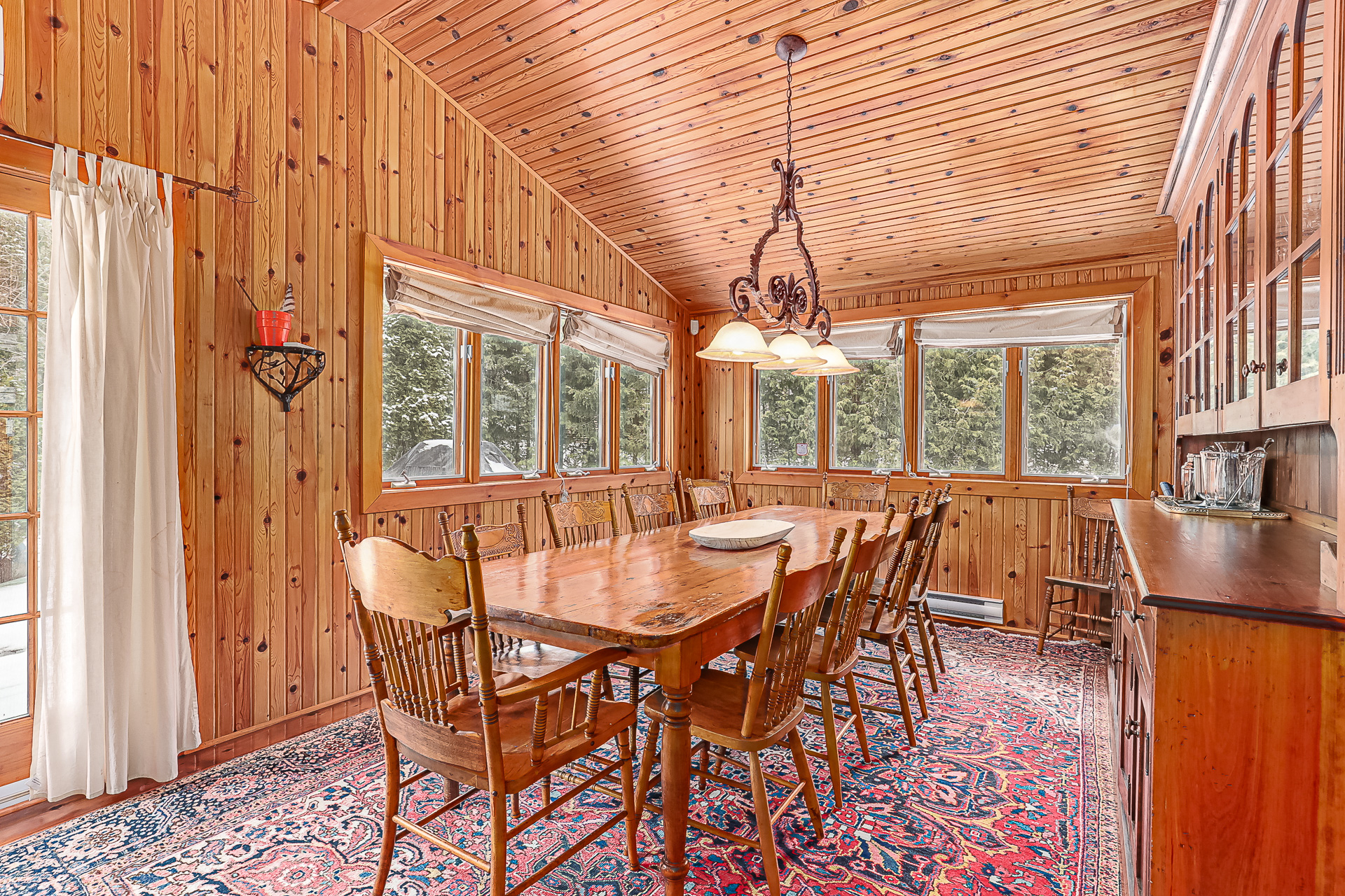 A dining table with wood chairs on a red patterned rug