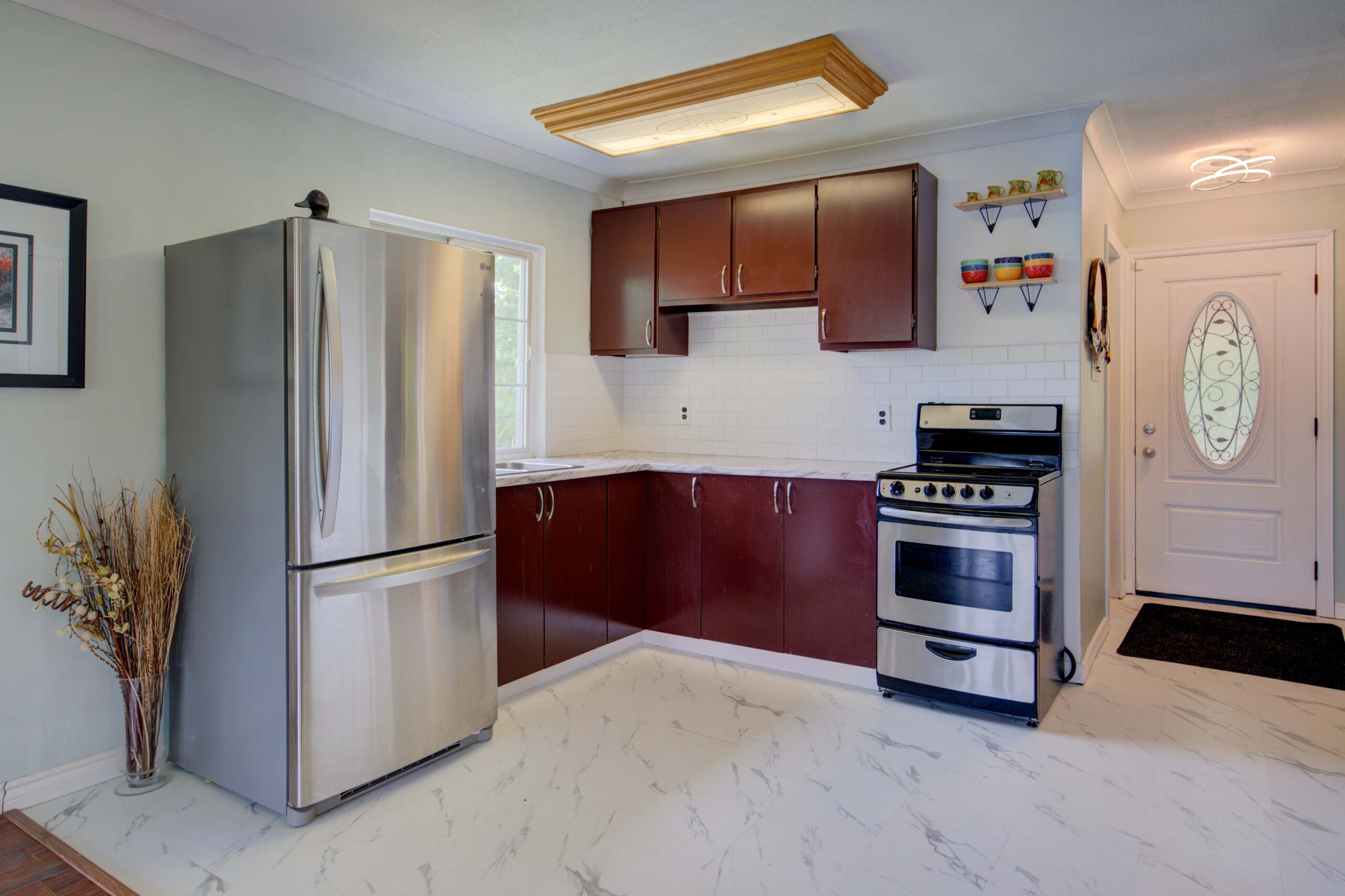A small white kitchen with red-brown cabinets and stainless steel appliances