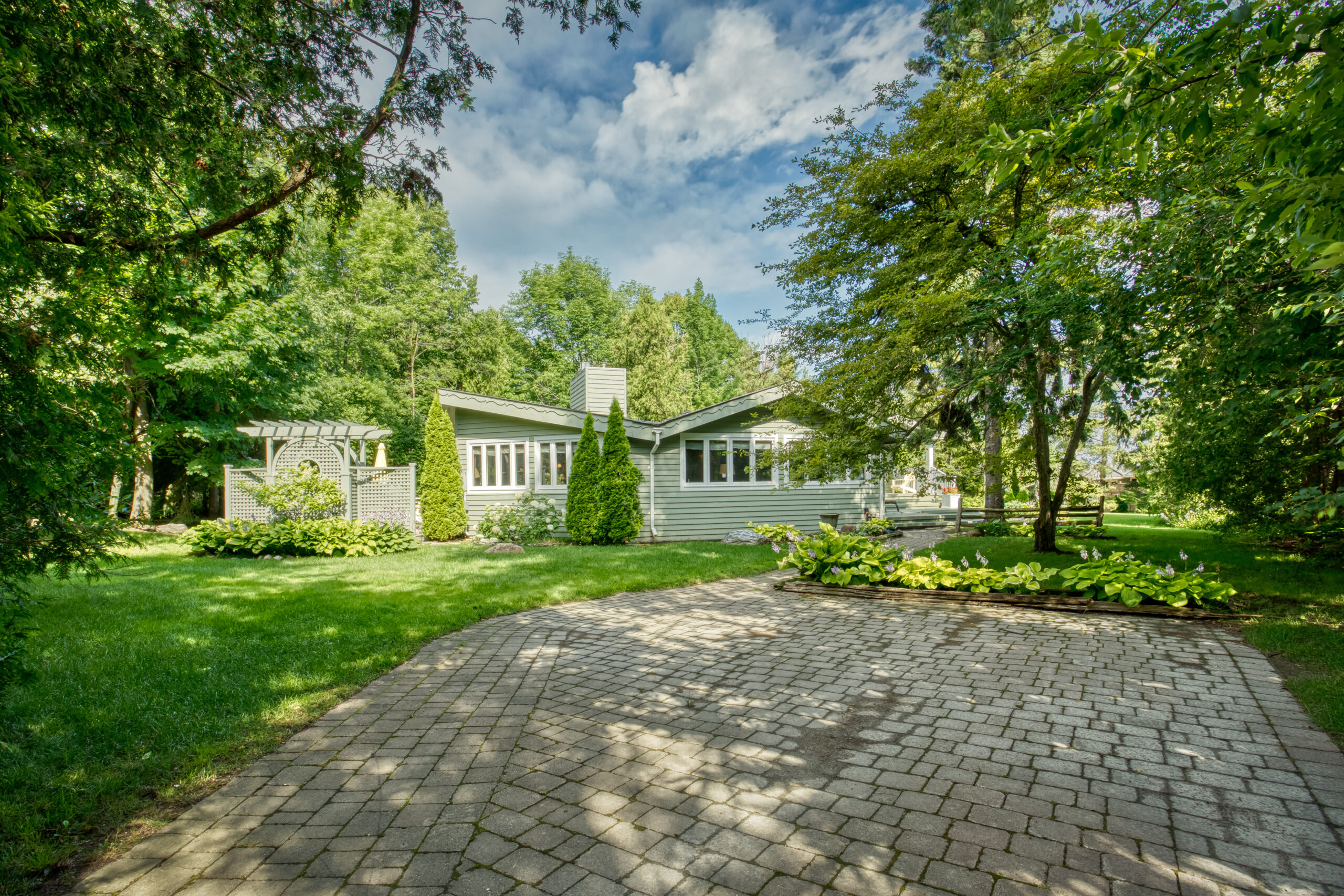 A green paneled cottage in a grassy green yard with a stone patio