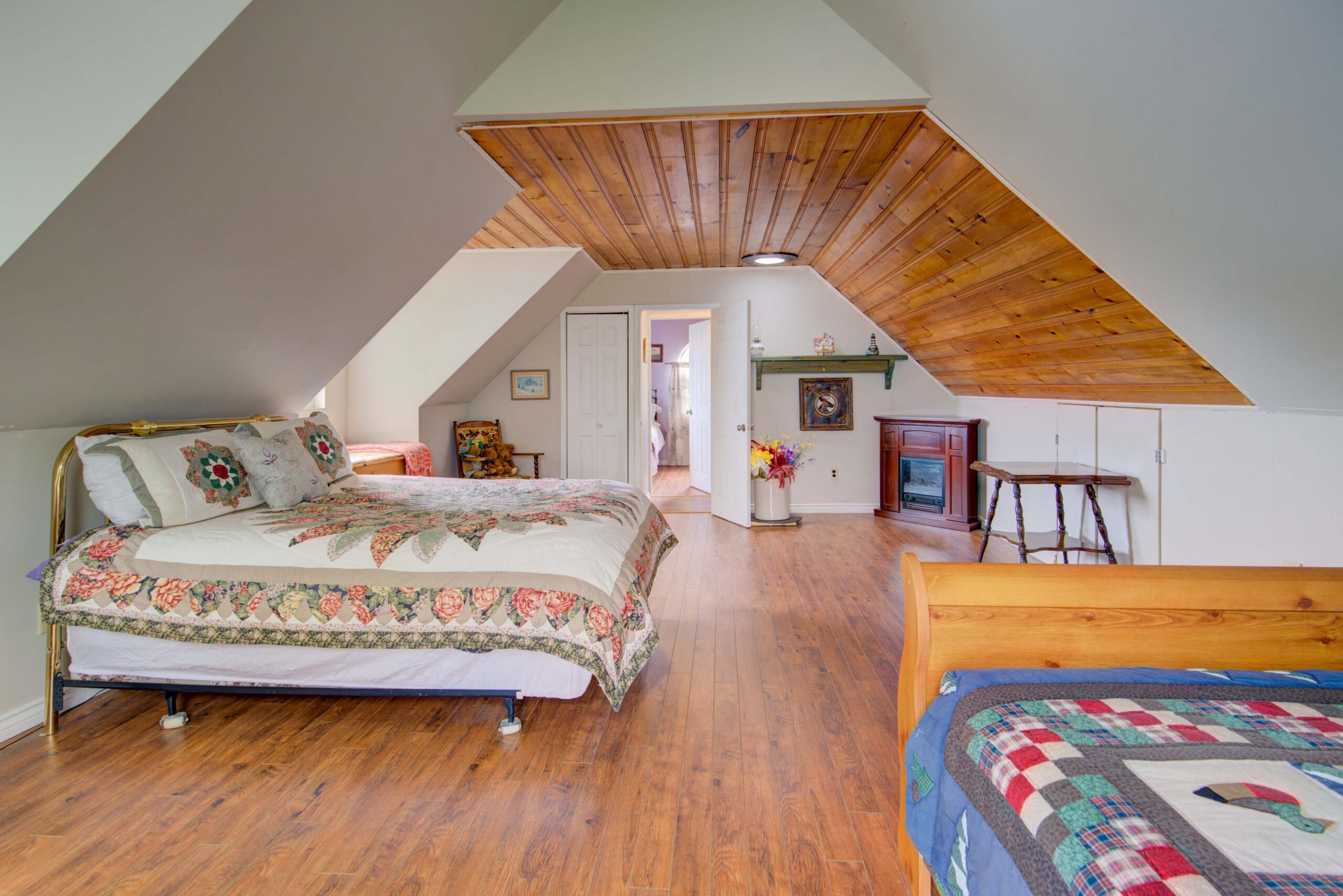 A quilted bed on the right faces a forward-facing bed in an attic room