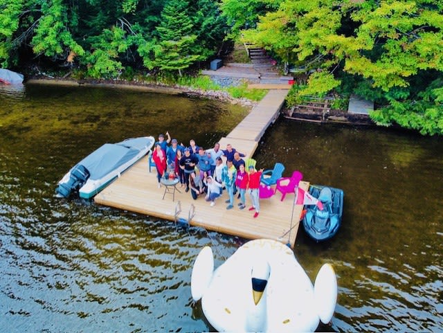 A large group of people standing at the edge of a dock. An inflatable swan floats in front