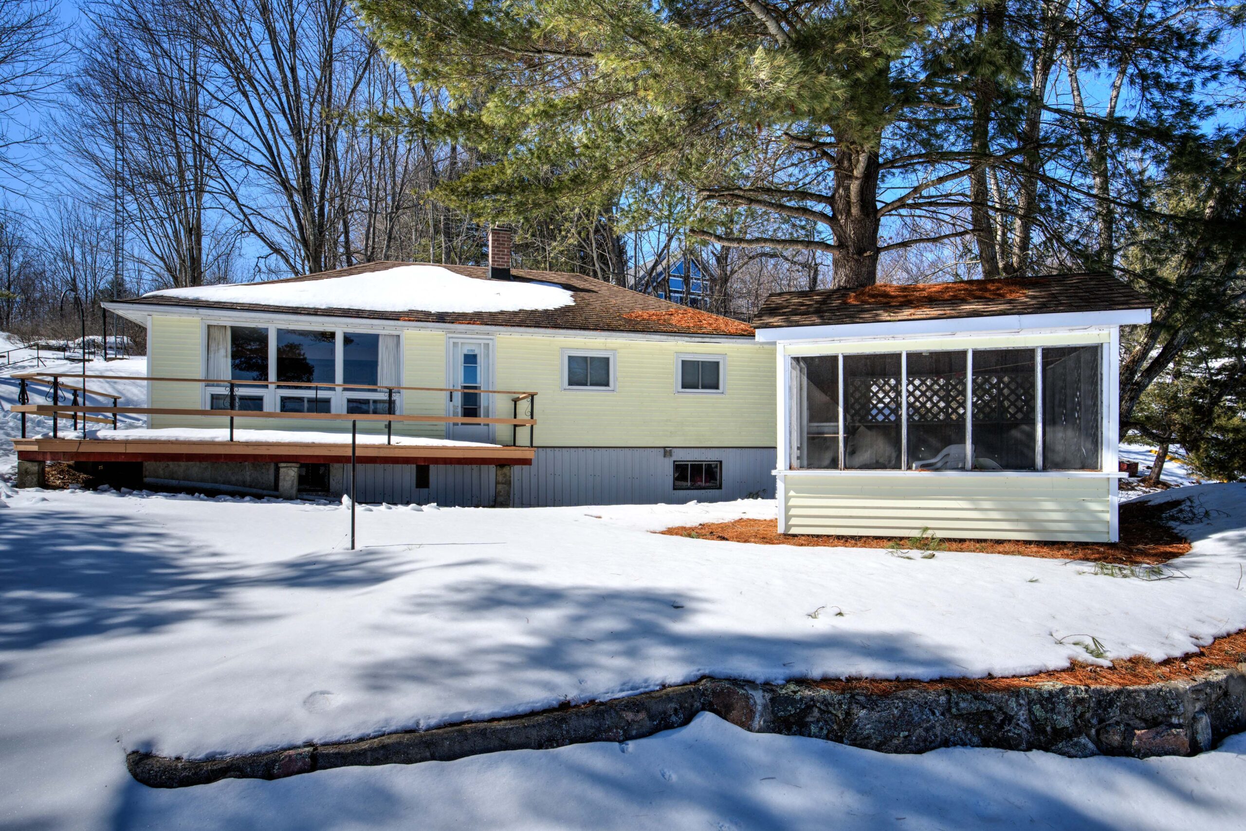 A light yellow cottage with a brown deck. Next door, a small yellow gazebo.