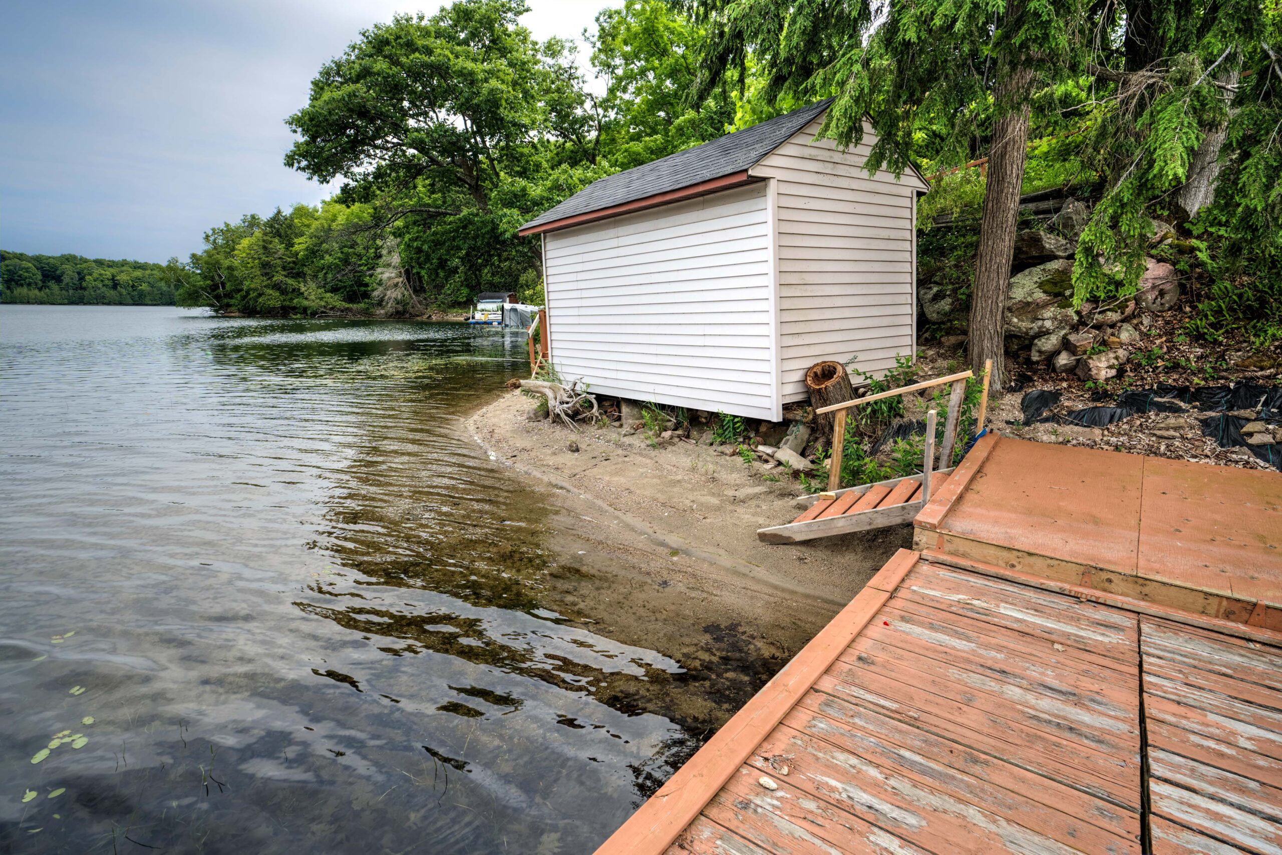A white wood-paneled shed with a brown door by the sandy beach