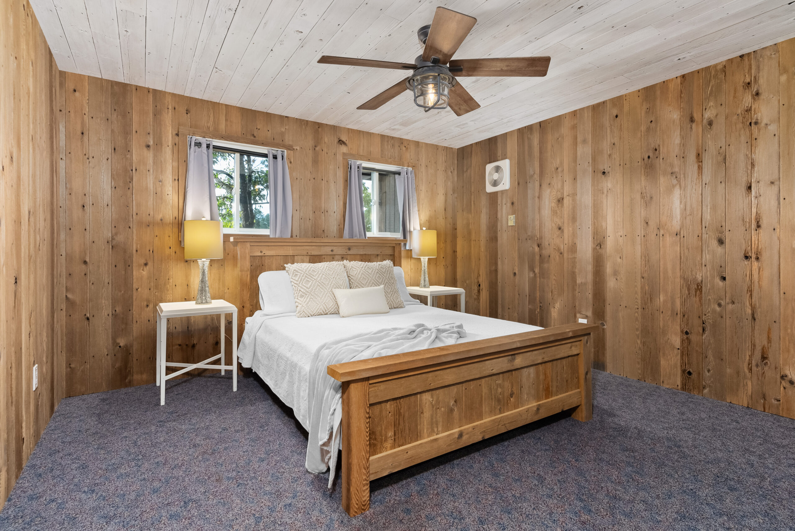 Guest bedroom with wood-paneled walls, ceiling fan, and a queen-sized bed.