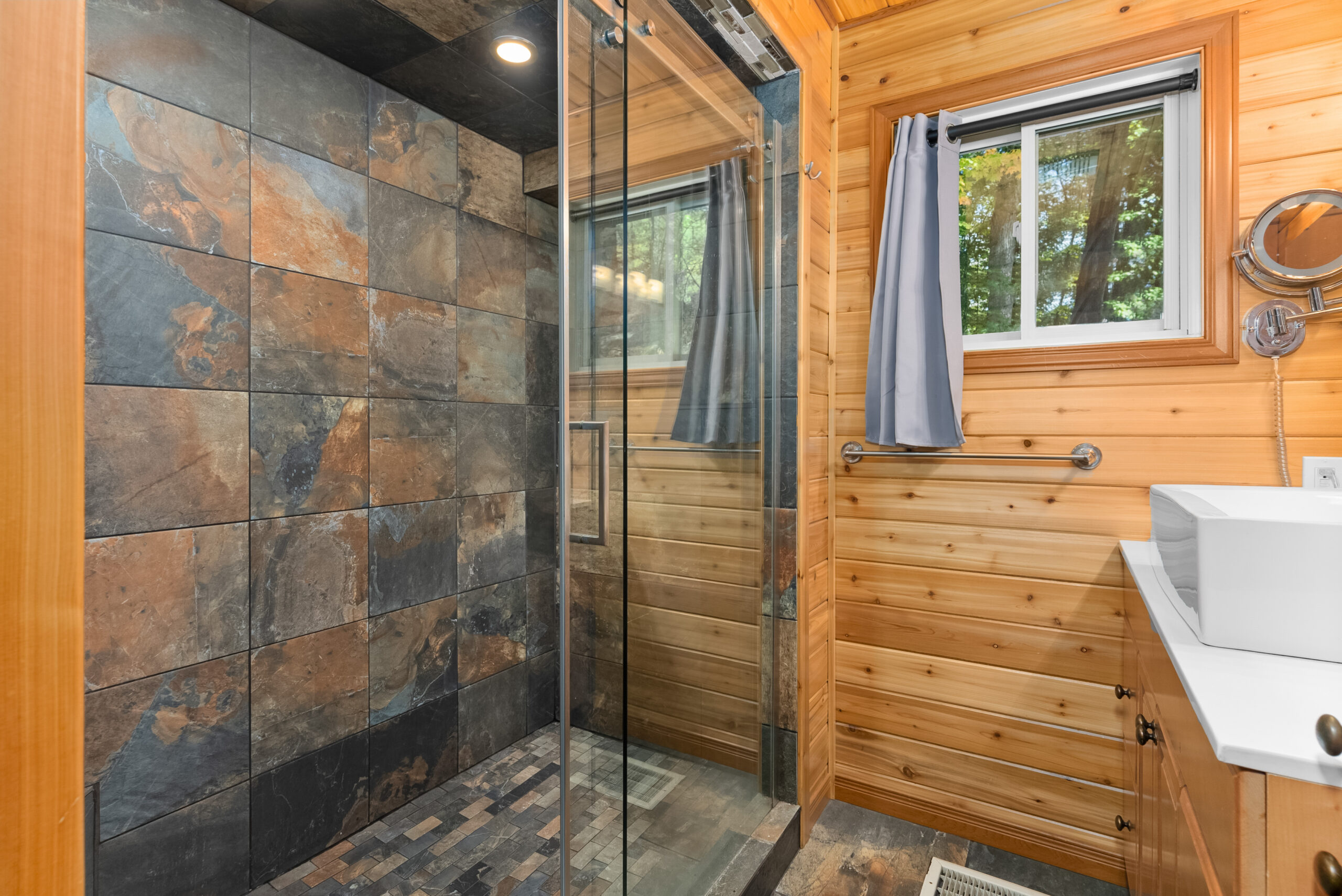 Bathroom with large walk-in shower, slate tile, and wooden accents.